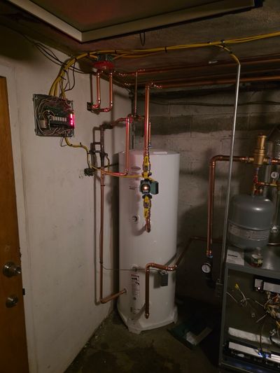 Modern water heater with copper manifold, electrical panel, and clean basement plumbing — recent E&GJ install.